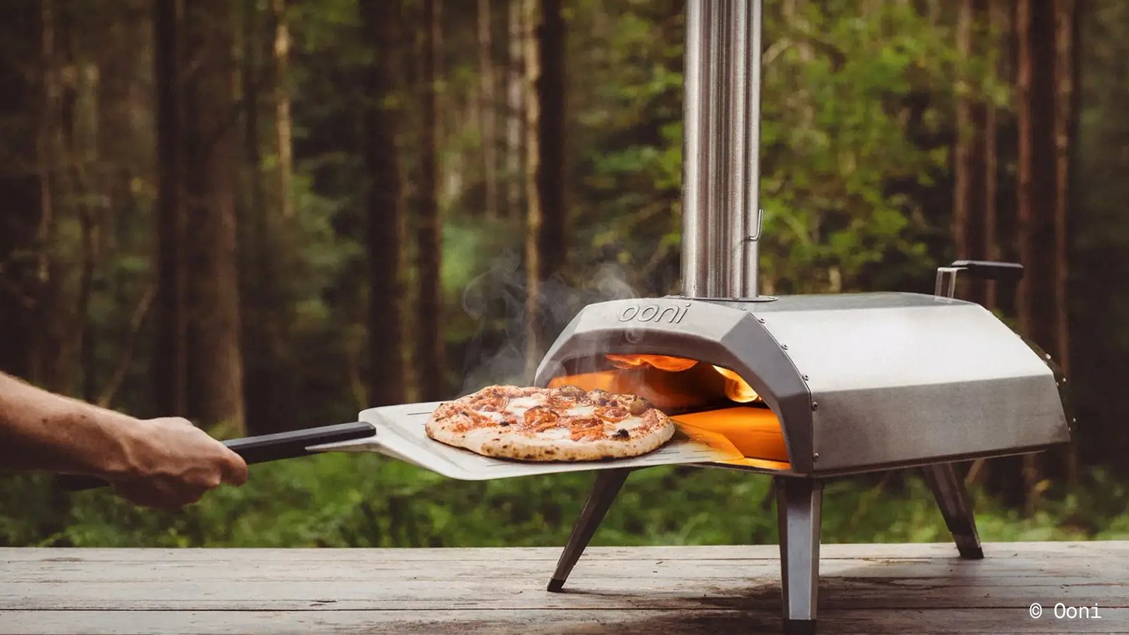 hand putting pizza in Ooni oven